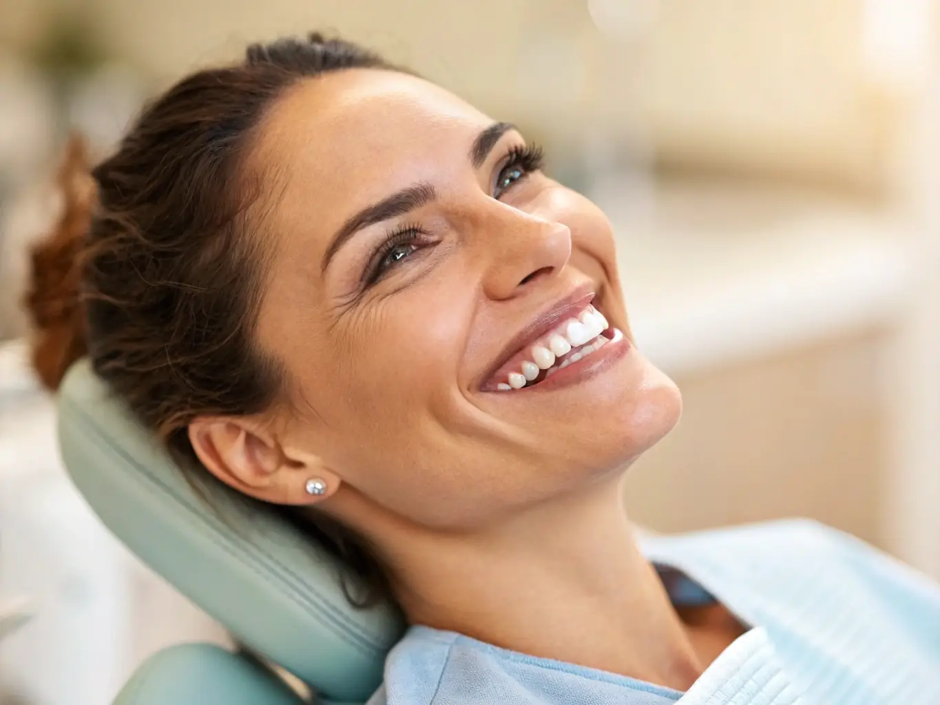 A close-up shot of a patient smiling confidently after receiving dental implants, showcasing natural-looking teeth and restored function. The background is a modern dental office setting.